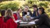 A group of smiling students around a laptop at an outdoor table
